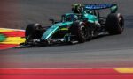 Teal Formula 1 race car taking a sharp turn on a race track with red and yellow curbs visible in the foreground.