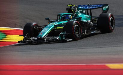 Teal Formula 1 race car taking a sharp turn on a race track with red and yellow curbs visible in the foreground.