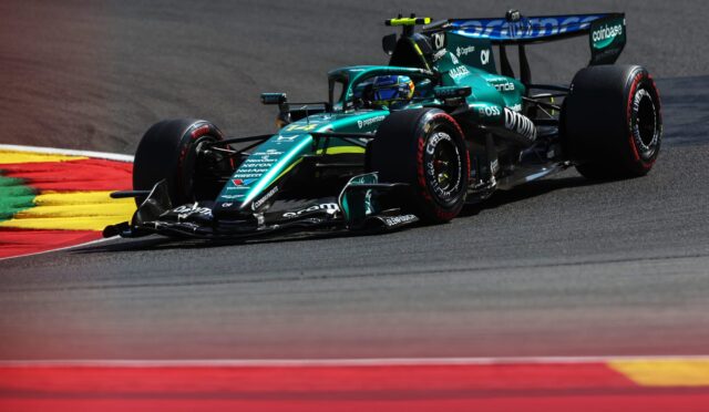 Teal Formula 1 race car taking a sharp turn on a race track with red and yellow curbs visible in the foreground.