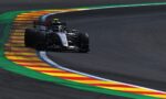 Formula 1 car hugging a left-hand corner on a dark race track, riding along the colorful striped curbs (green, yellow, red).