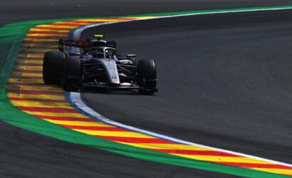 Formula 1 car hugging a left-hand corner on a dark race track, riding along the colorful striped curbs (green, yellow, red).