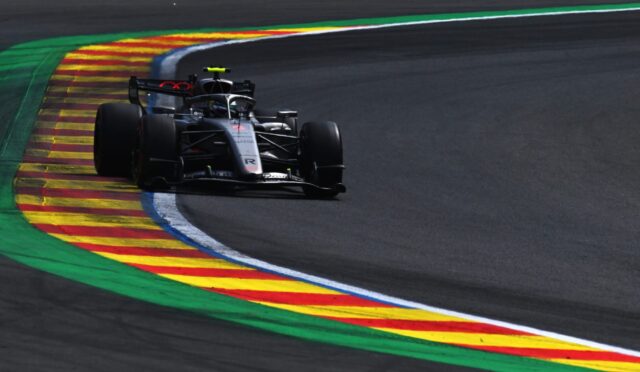 Formula 1 car hugging a left-hand corner on a dark race track, riding along the colorful striped curbs (green, yellow, red).