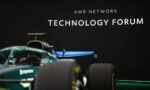 Race car in the foreground with a black wall displaying 'AMR NETWORK TECHNOLOGY FORUM' in the background.