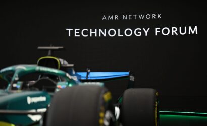Race car in the foreground with a black wall displaying 'AMR NETWORK TECHNOLOGY FORUM' in the background.
