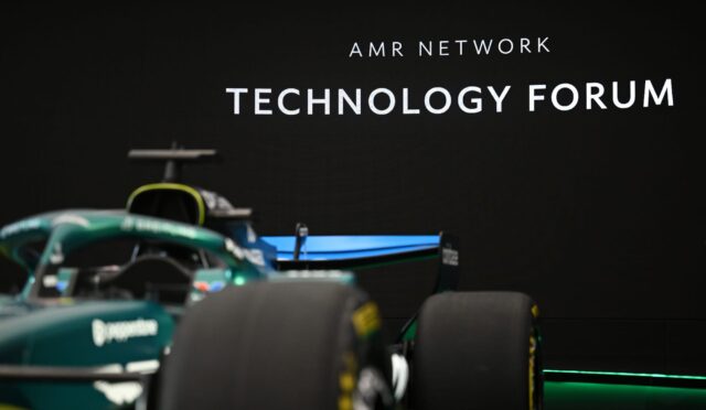 Race car in the foreground with a black wall displaying 'AMR NETWORK TECHNOLOGY FORUM' in the background.