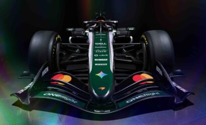 Front view of a dark green Formula 1 race car with sponsor logos and rainbow reflections in a studio setting.