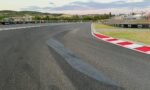 Wide view of a race track curve with red-and-white curbs, safety barriers, and empty spectator fencing under a blue sky