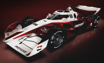IndyCar race car in white and red livery, shown from a front-left angle against a dark red background, with INDYCAR branding visible.