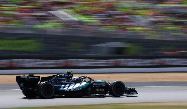 Mercedes-AMG Petronas Formula One car speeding on the track with blurred grandstands in the background, sponsor logos visible below.