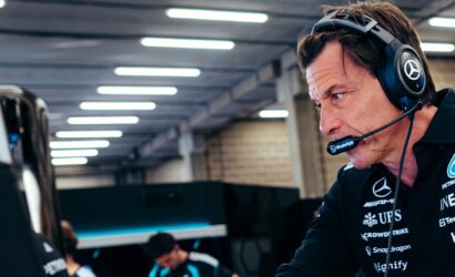 Male esports team member wearing a headset and mic, focused on a computer screen in a tech workspace, with branded polo.