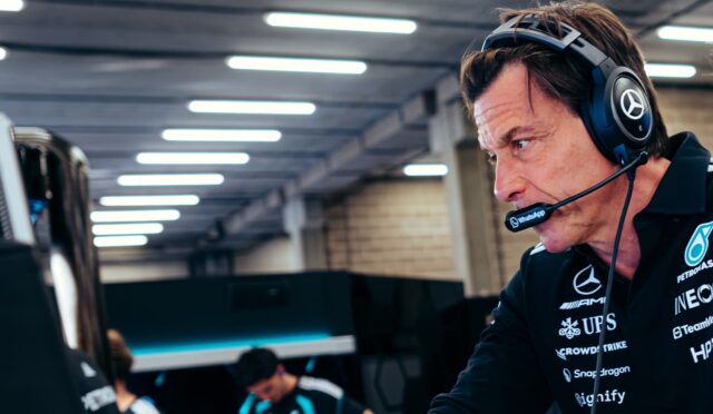 Male esports team member wearing a headset and mic, focused on a computer screen in a tech workspace, with branded polo.