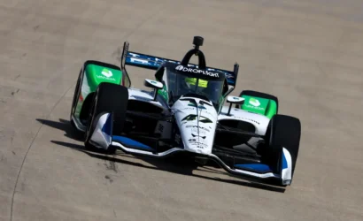 Open-wheel race car on a track, white with green accents and sponsor logos visible on the body and rear wing.