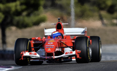 Red Formula 1 race car on a track, front view with a blue-helmeted driver visible.