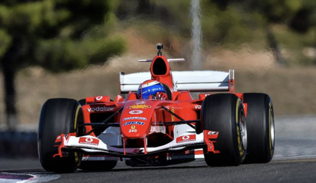 Red Formula 1 race car on a track, front view with a blue-helmeted driver visible.