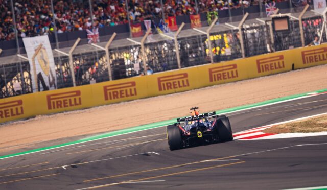 Formula 1 car racing on a track with yellow Pirelli barriers and a cheering grandstand in the background