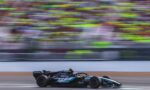 Formula 1 car speeding along a race track with colorful, blurred grandstands in the background.