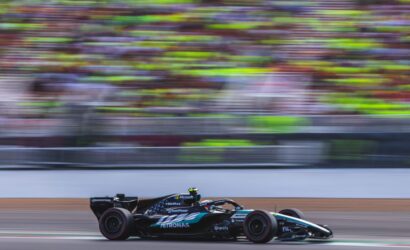 Formula 1 car speeding along a race track with colorful, blurred grandstands in the background.