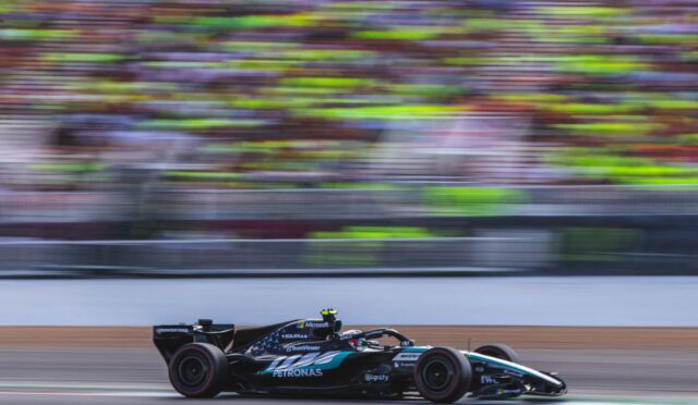 Formula 1 car speeding along a race track with colorful, blurred grandstands in the background.