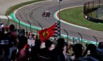 Red Formula 1 car speeds around a curve with cheering fans behind a fence.