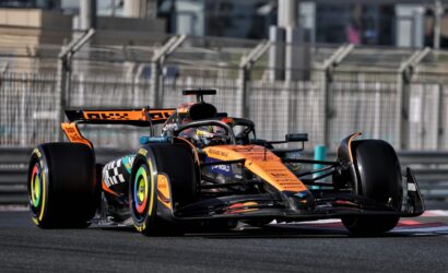 Orange Formula 1 car racing on a track with safety barriers in the background, front and wheel visible in motion.