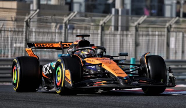 Orange Formula 1 car racing on a track with safety barriers in the background, front and wheel visible in motion.