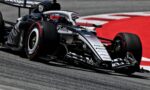 Race car speeding on track; close-up of front wing and slick tire with red run-off in the background. (informative)