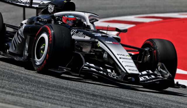 Race car speeding on track; close-up of front wing and slick tire with red run-off in the background. (informative)