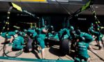 Aston Martin Formula 1 pit crew in teal suits service a race car in the pit lane.