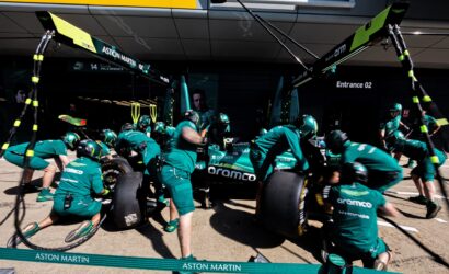 Aston Martin Formula 1 pit crew in teal suits service a race car in the pit lane.