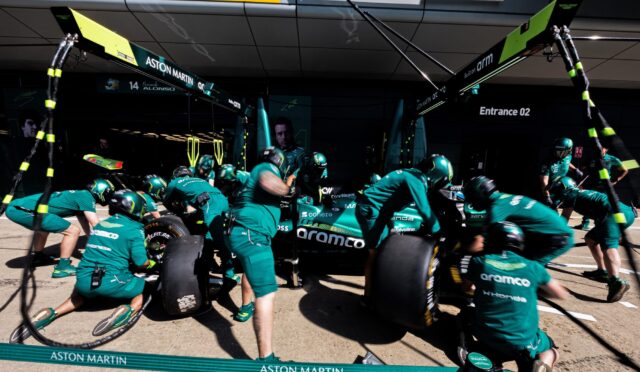 Aston Martin Formula 1 pit crew in teal suits service a race car in the pit lane.