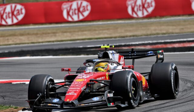 Red Ferrari Formula 1 car speeds around a bend on a race track, with sponsor banners along a red barrier in the background.