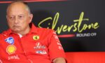 Close-up of an older man in a red Ferrari jacket at a media event, sponsor logos visible on his chest.