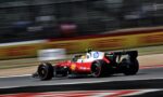 Red Formula 1 car in motion on a race track with sponsor logos and blurred background barriers.