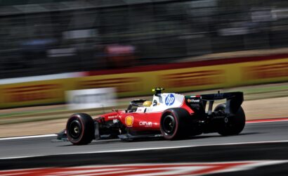 Red Formula 1 car in motion on a race track with sponsor logos and blurred background barriers.
