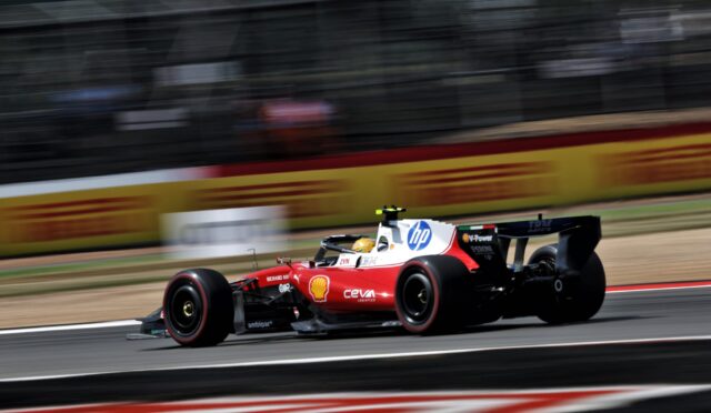 Red Formula 1 car in motion on a race track with sponsor logos and blurred background barriers.