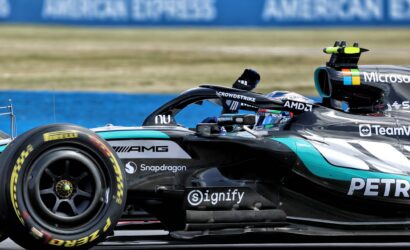 Close-up of a Formula 1 car's side with sponsor logos (Microsoft, AMD) and a Pirelli tire on a race track barrier in the background.