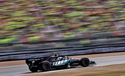 Formula 1 car in Petronas livery speeds along the track as colorful grandstands blur in the background.