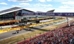 Formula 1 race start on a sunlit circuit with numerous spectators, cars lined up behind the start banner and track barriers branded Pirelli and Las Vegas.