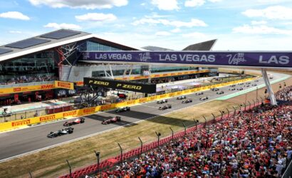 Formula 1 race start on a sunlit circuit with numerous spectators, cars lined up behind the start banner and track barriers branded Pirelli and Las Vegas.