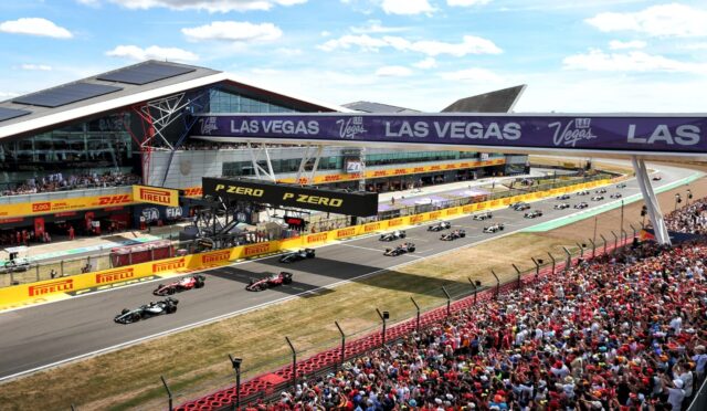 Formula 1 race start on a sunlit circuit with numerous spectators, cars lined up behind the start banner and track barriers branded Pirelli and Las Vegas.