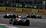 Formula 1 cars race on track near advertising banners, front car USA livery leading a pack