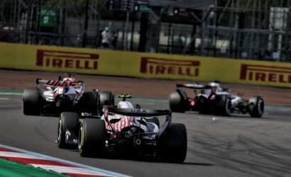 Formula 1 cars race on track near advertising banners, front car USA livery leading a pack