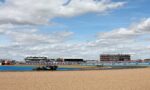 Black Formula 1 car speeding along a track with gravel in the foreground and grandstands full of spectators in the distance under a partly cloudy sky.