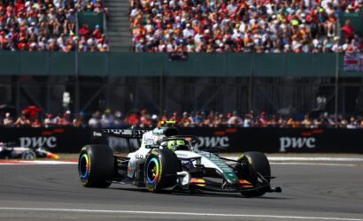 Formula 1 car speeding along the track with a packed grandstand crowd in the background near the pit wall nearby the stands.