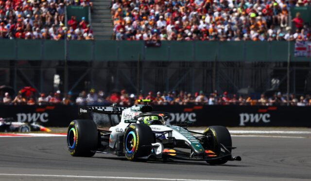 Formula 1 car speeding along the track with a packed grandstand crowd in the background near the pit wall nearby the stands.
