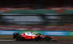 Red Formula 1 car number 44 speeding on a race track with blurred grandstands in the background, motion blur conveying speed.