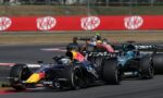 Red Bull Racing leads a pack of Formula 1 cars around a bend on the race track with red KitKat banners in the background.