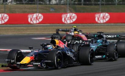 Red Bull Racing leads a pack of Formula 1 cars around a bend on the race track with red KitKat banners in the background.