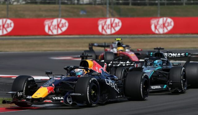 Red Bull Racing leads a pack of Formula 1 cars around a bend on the race track with red KitKat banners in the background.