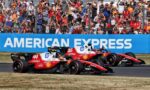 Two red Ferrari Formula 1 cars race side by side on track as a cheering crowd watches behind a chain-link fence and a blue barrier reading American Express.